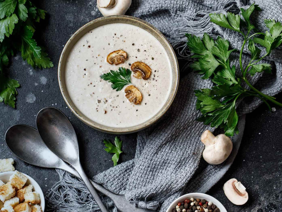 A bowl of creamy mushroom soup garnished with fresh garlic and parsley, showcasing a rich and inviting texture.